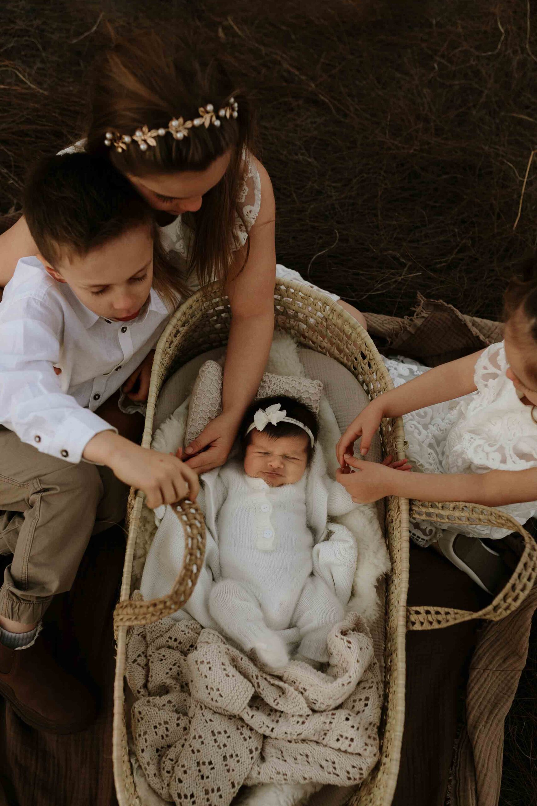 Adelaide siblings looking at their new baby sister in a mosses basket.
