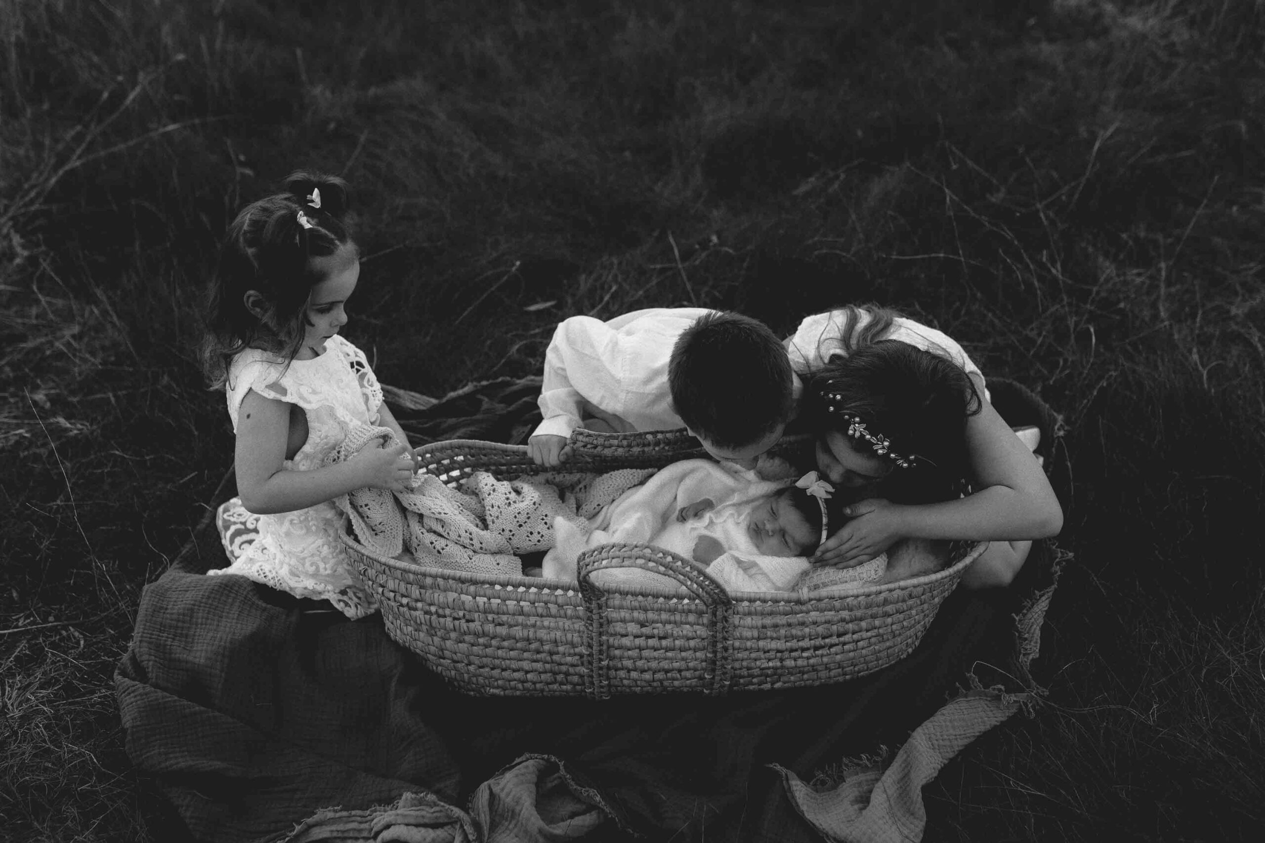 Adelaide siblings looking at their new baby sister in a mosses basket.