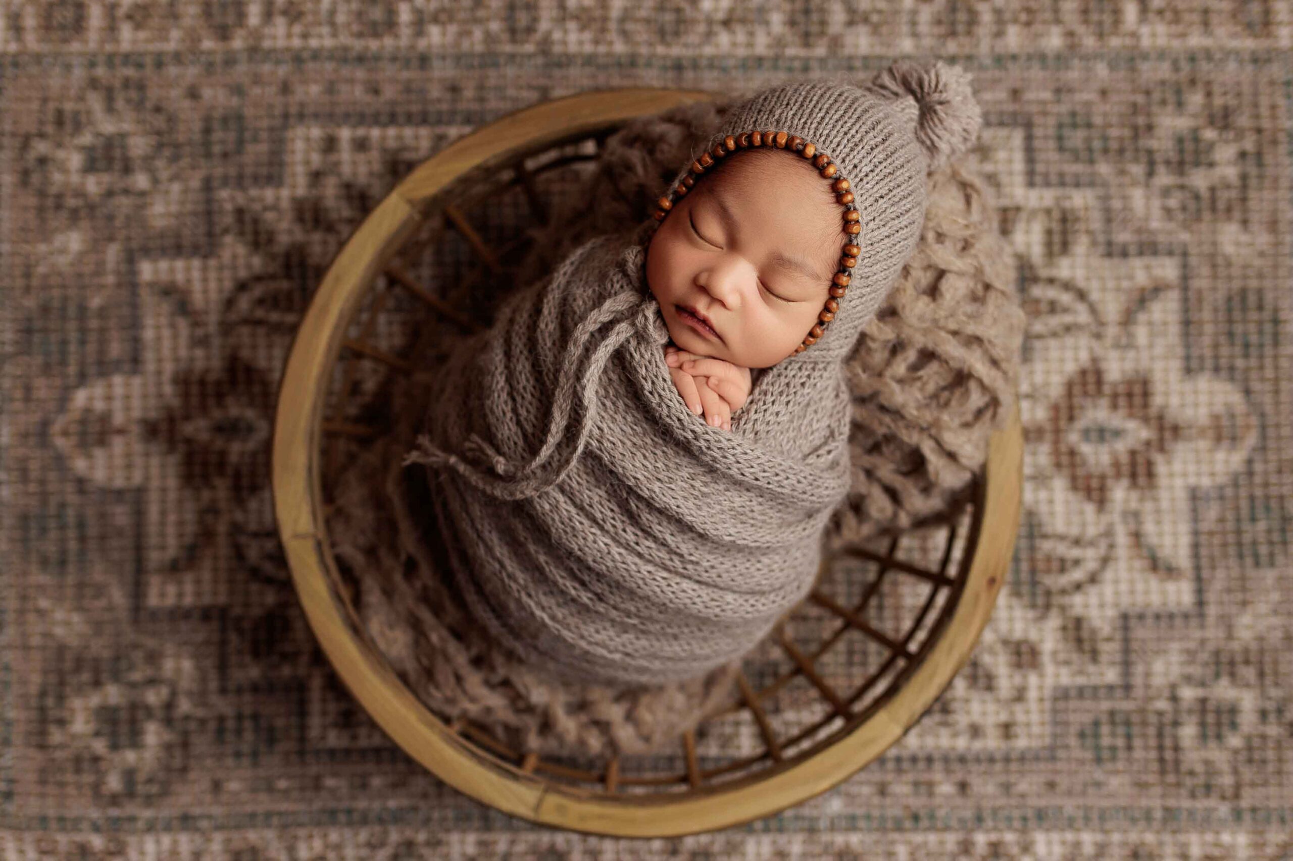 An Adelaide newborn baby wrapped and wearing a bonnet asleep in a bowl.