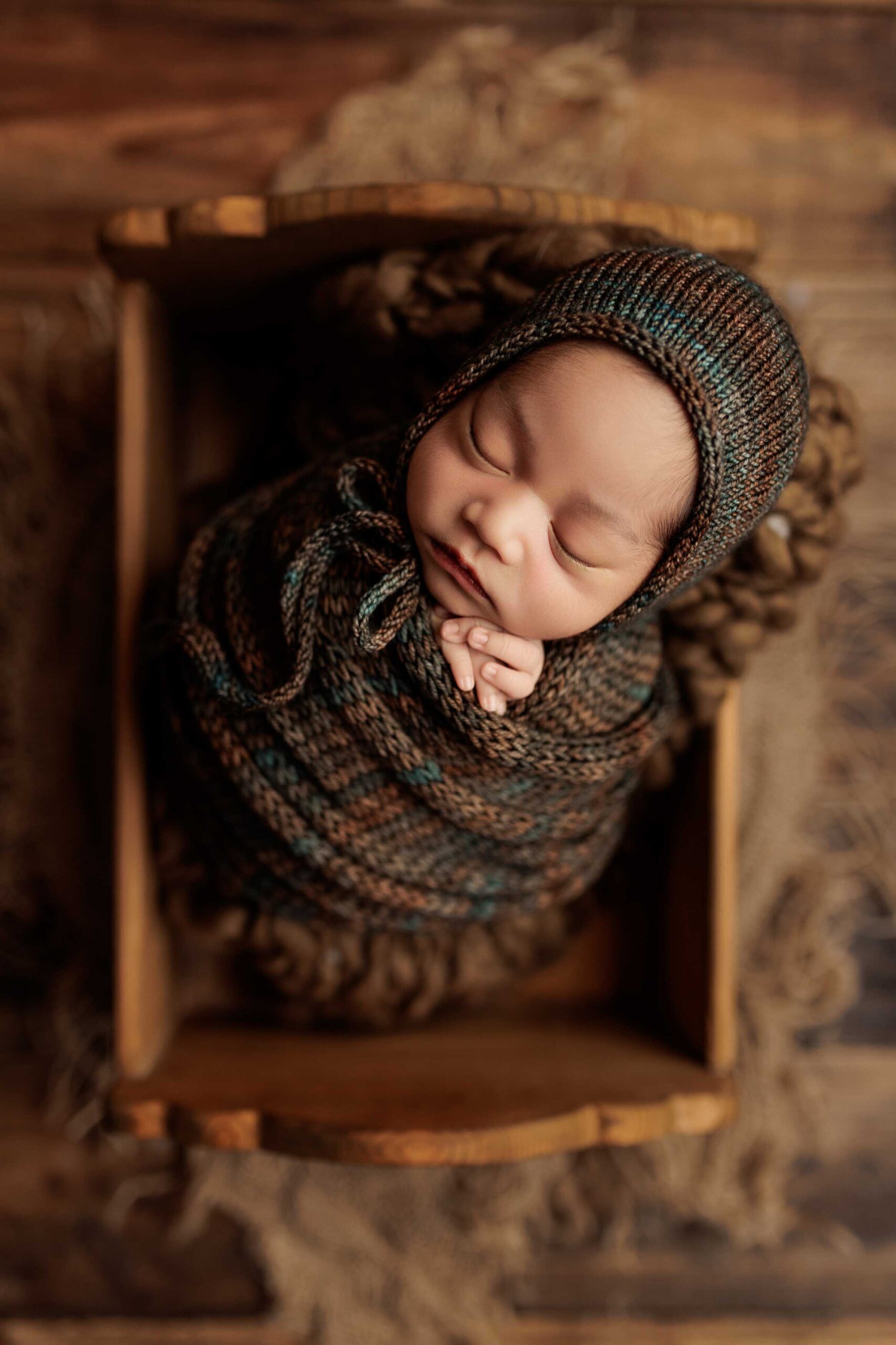 An Adelaide baby in a wrap and bonnet asleep in a crate.