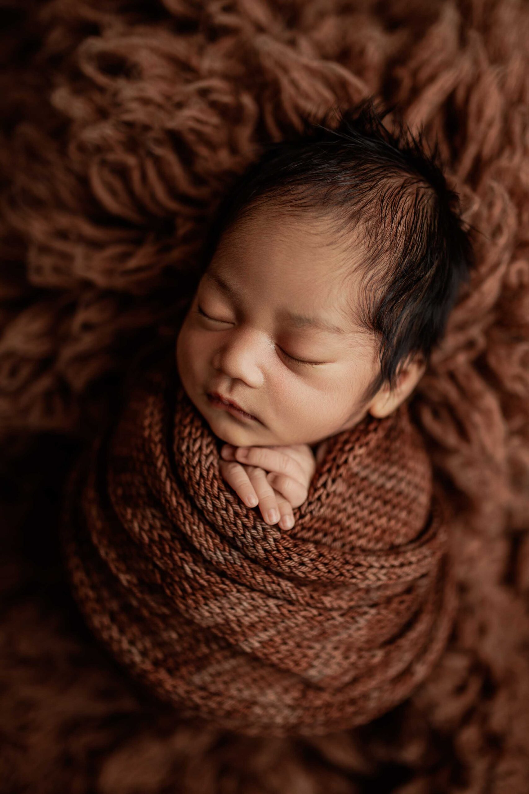 An Adelaide baby wrapped and  asleep in a brown fur rug.