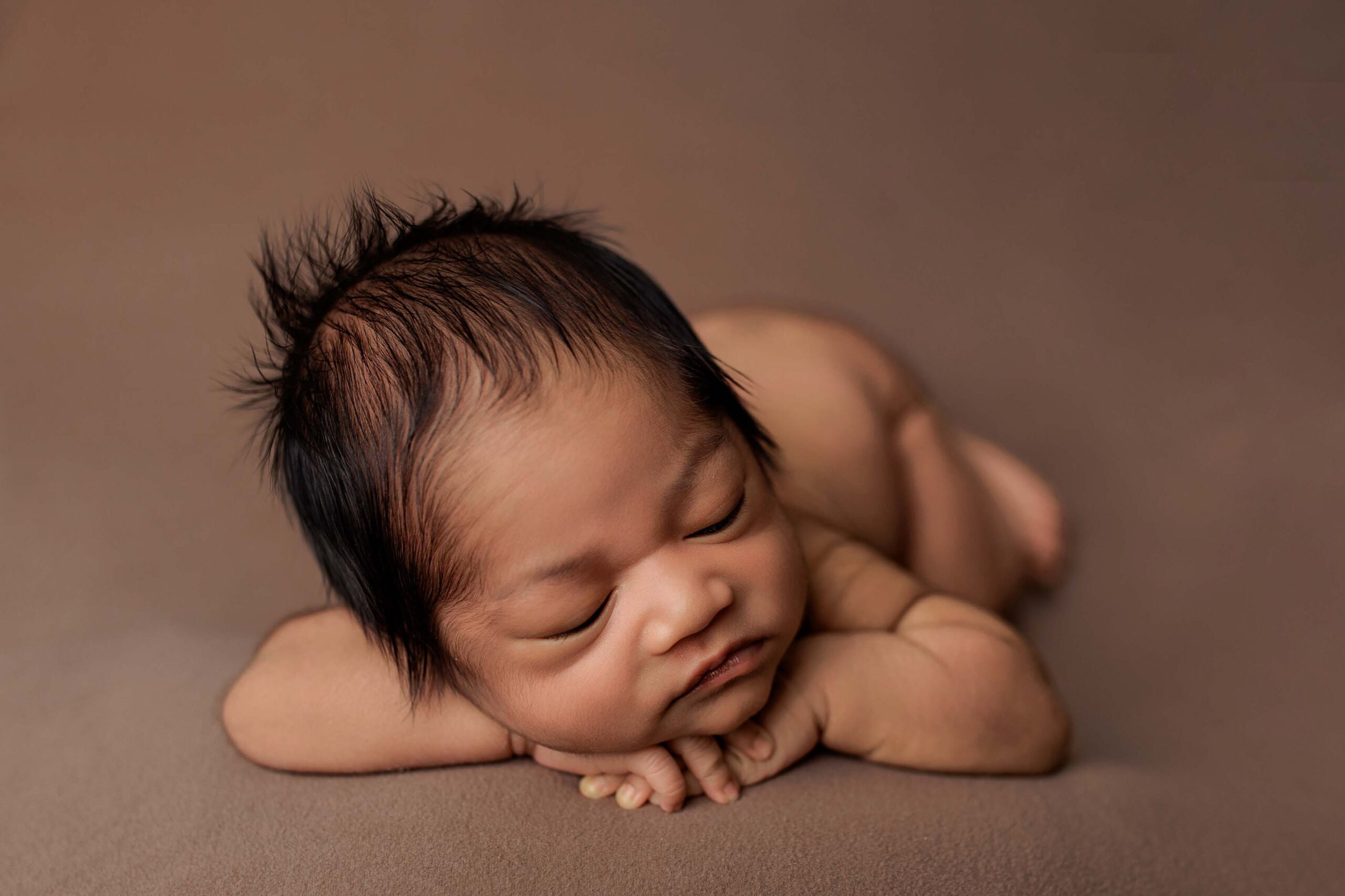 A newborn baby from the Adelaide hills asleep on a brown blanket.