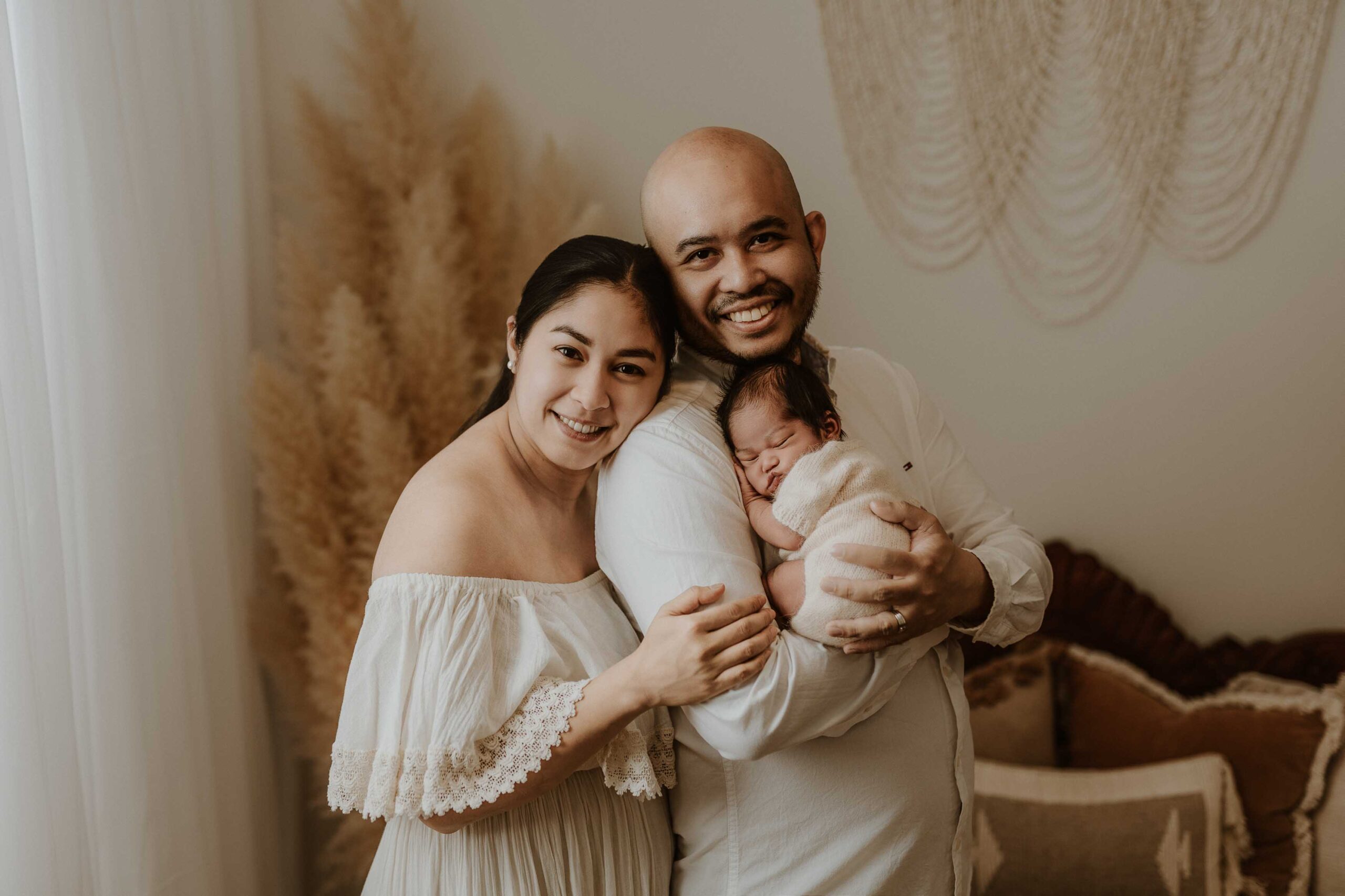 A couple in an Adelaide newborn photography studio smiling while holding their new baby.
