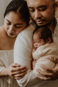 A closeup of a couple in an Adelaide newborn photography studio hugging while holding their new baby.