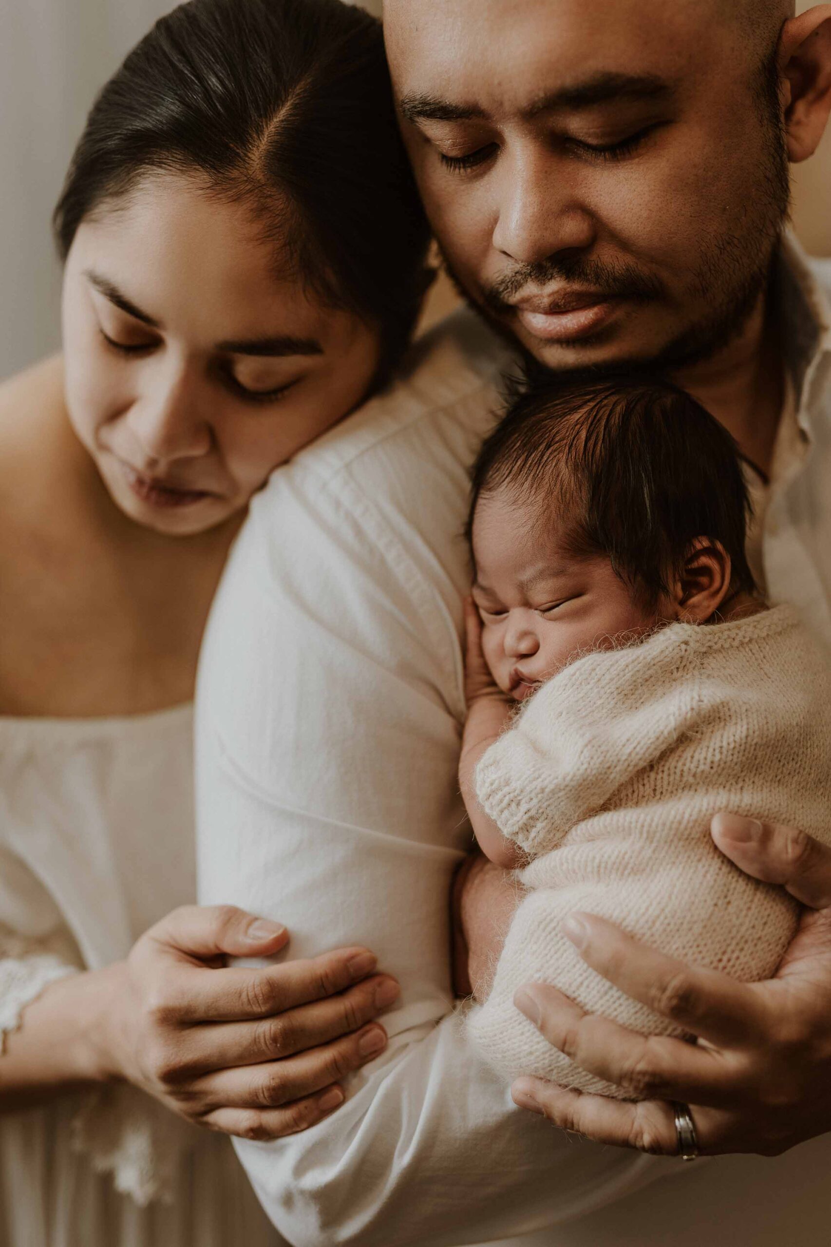 A closeup of a couple in an Adelaide newborn photography studio hugging while holding their new baby.