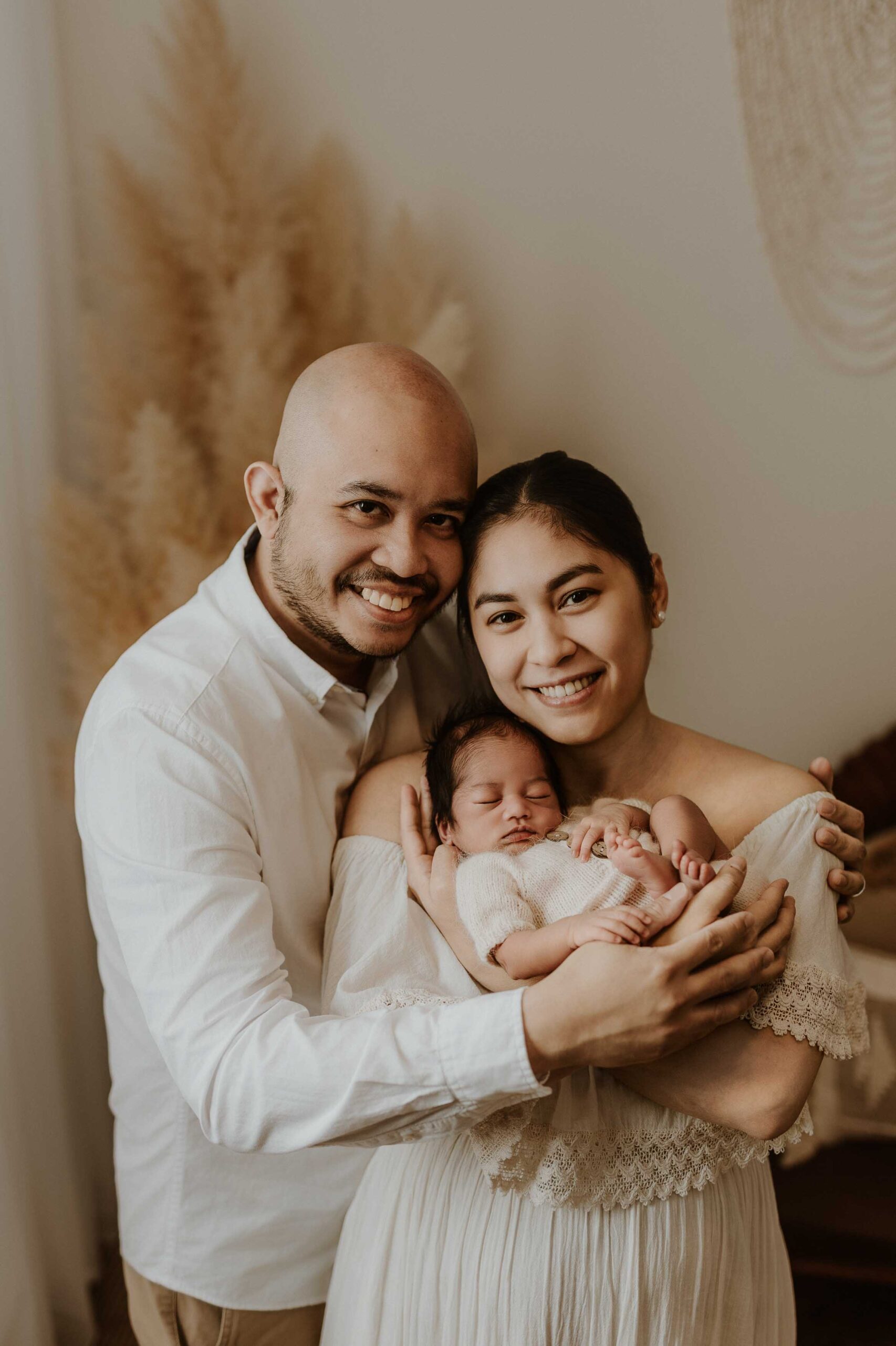 A couple in an Adelaide newborn photography studio smiling while holding their new baby.