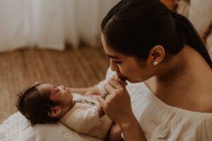 An Adelaide mum holding her newborn baby on her chest.lap and kissing his fingers.