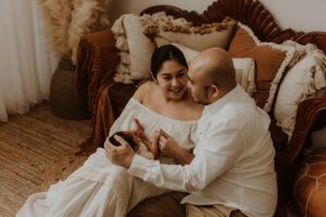 A couple in an Adelaide newborn photography studio sitting on the floor looking at each other while holding their new baby.