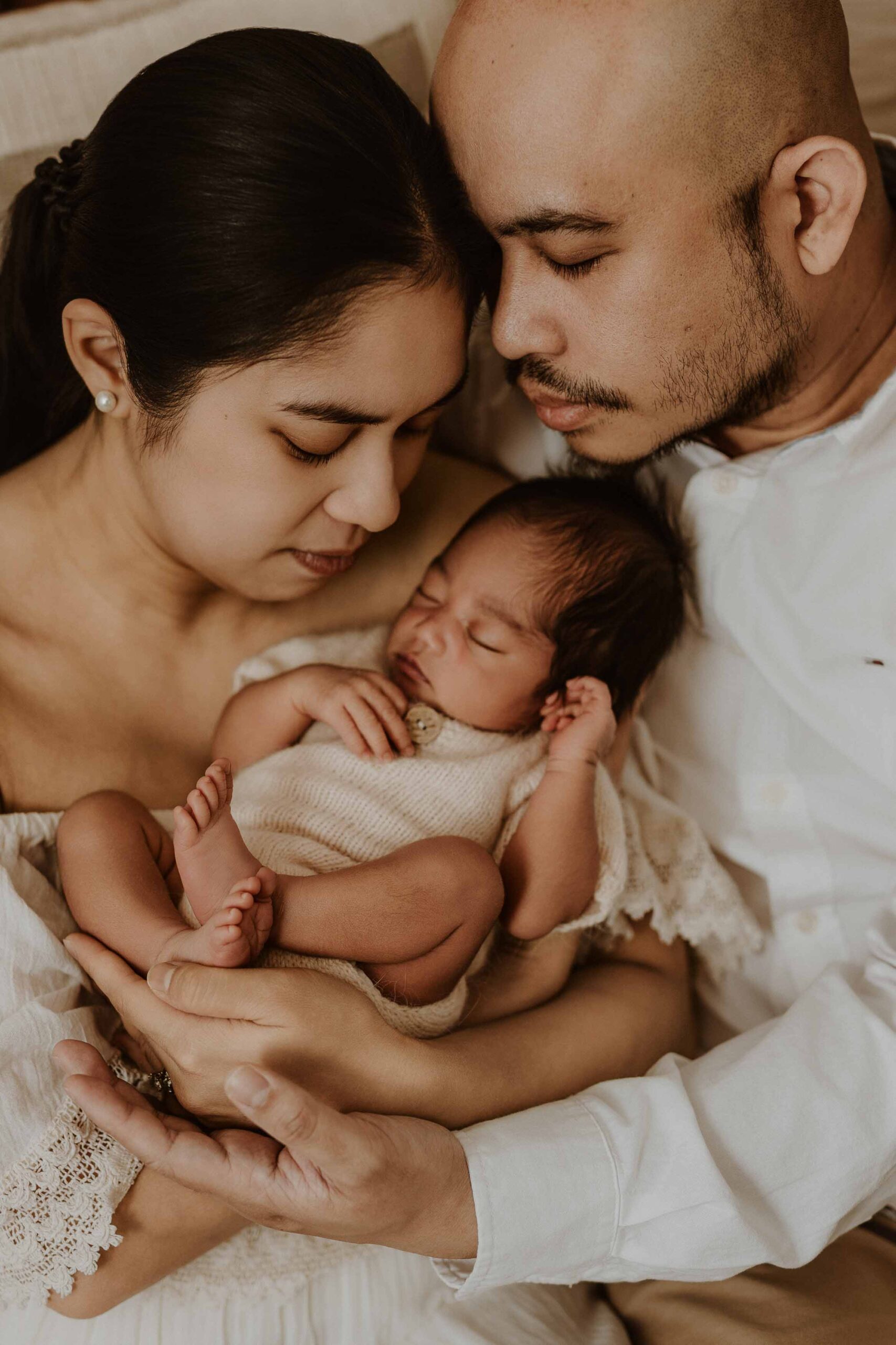 A couple in an Adelaide newborn photography studio sitting on the floor looking at their new baby.