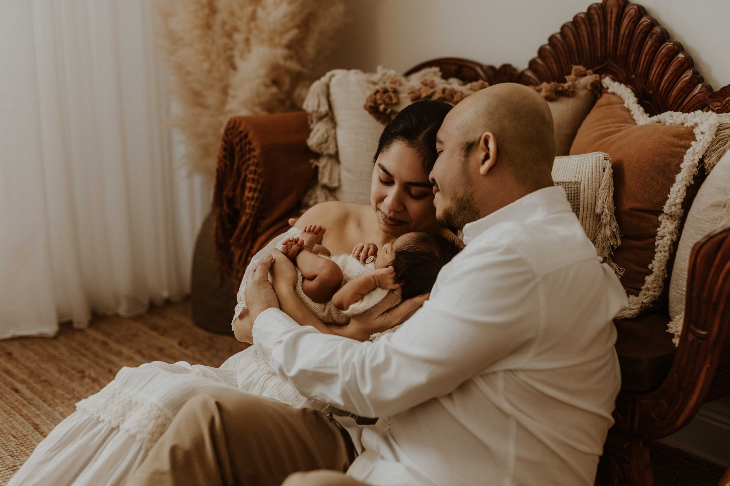 A couple in an Adelaide newborn photography studio sitting on the floor looking at their new baby.