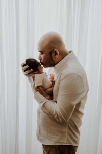 A backlit Adelaide dad holding his newborn baby.