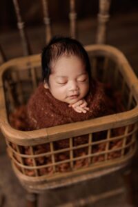 An Adelaide baby wrapped and posed upright in a crate on a chair.