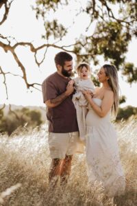 An Adelaide family standing next to a tree and hugging each other in a field.
