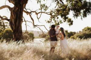 An Adelaide family standing next to a tree and hugging each other in a field.