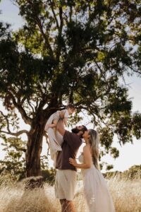 An Adelaide mother and father playing with their 8 month old son outside in a field.