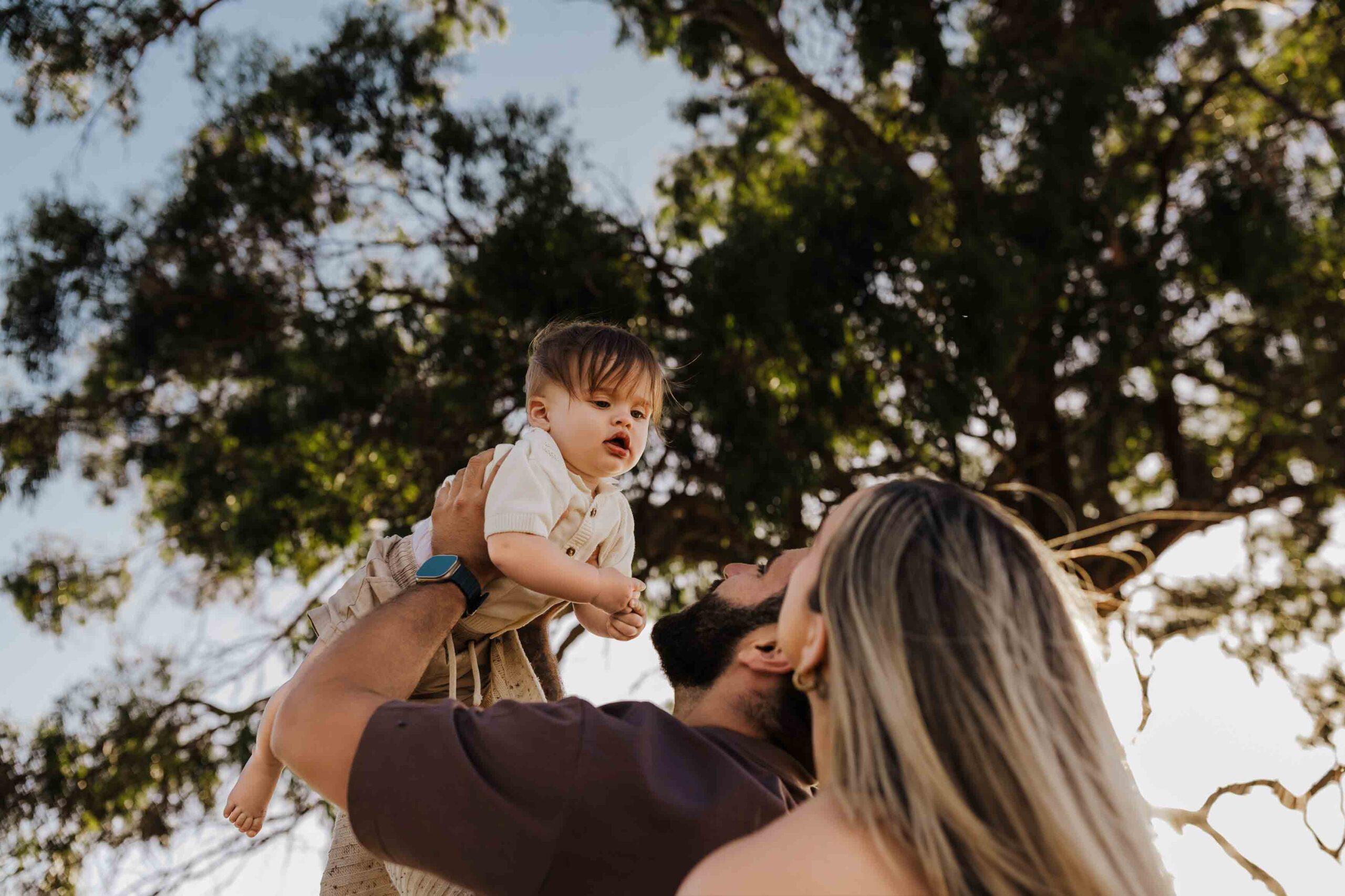 An Adelaide mother and father playing with their 8 month old son outside in a field.