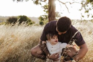 A dad from Adelaide playing in a field with his 8 month old baby son.