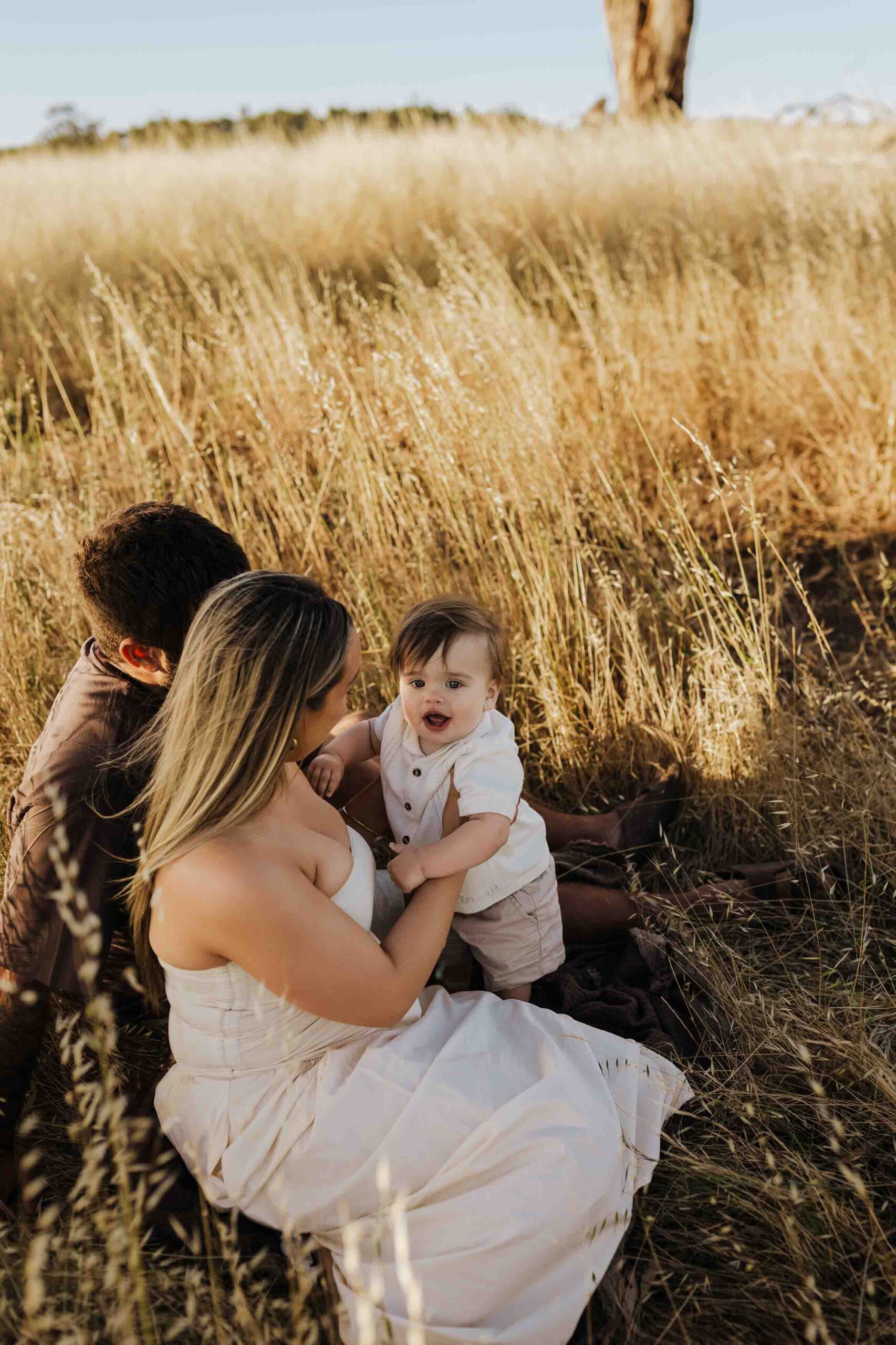 An Adelaide mother and father playing with their 8 month old son outside in a field.