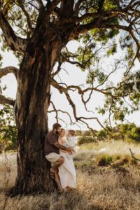 An Adelaide family standing next to a tree and hugging each other in a field.