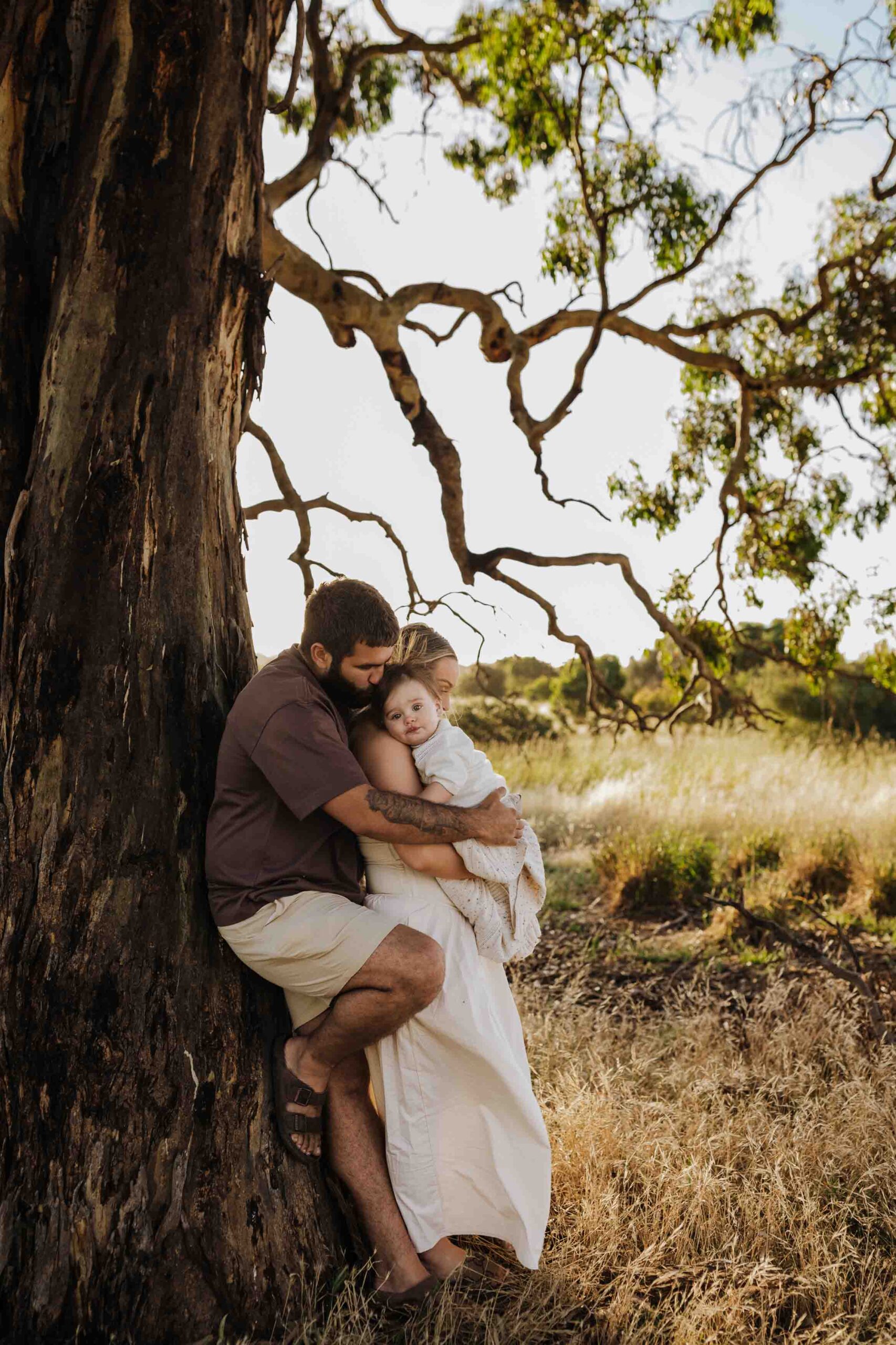 An Adelaide family standing next to a tree and hugging each other in a field.