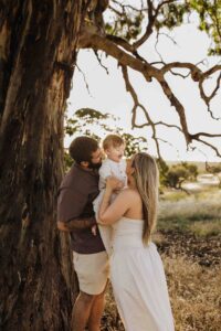 An Adelaide family standing next to a tree and hugging each other in a field.