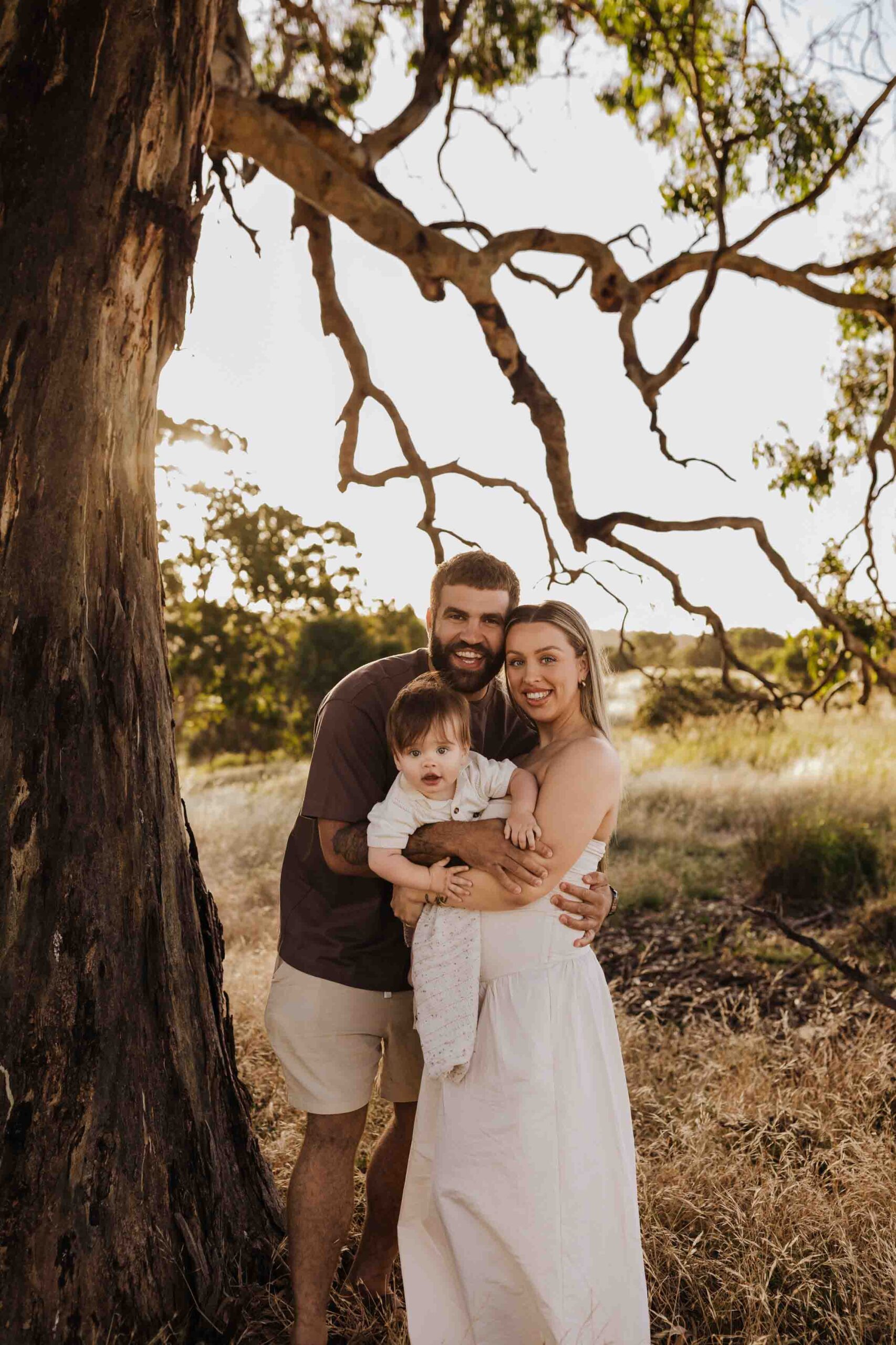 An Adelaide family standing next to a tree and hugging each other in a field.