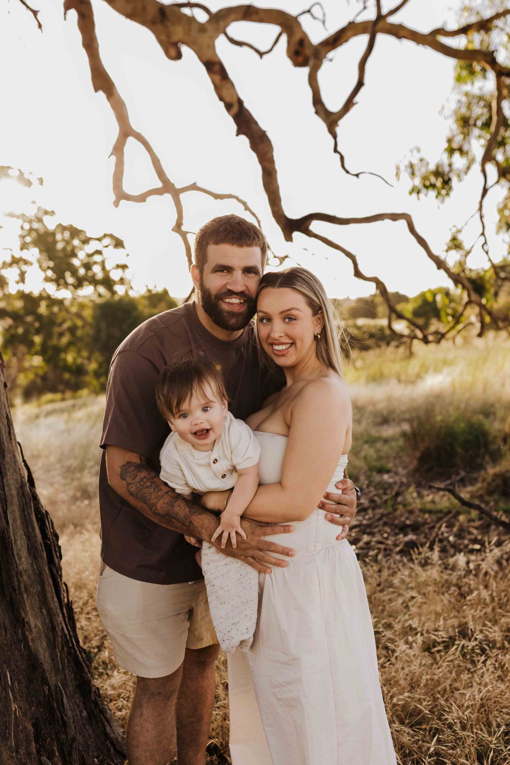 An Adelaide family standing next to a tree and hugging each other in a field.