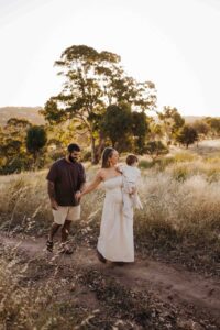 An Adelaide family of 3 walking together in a field.