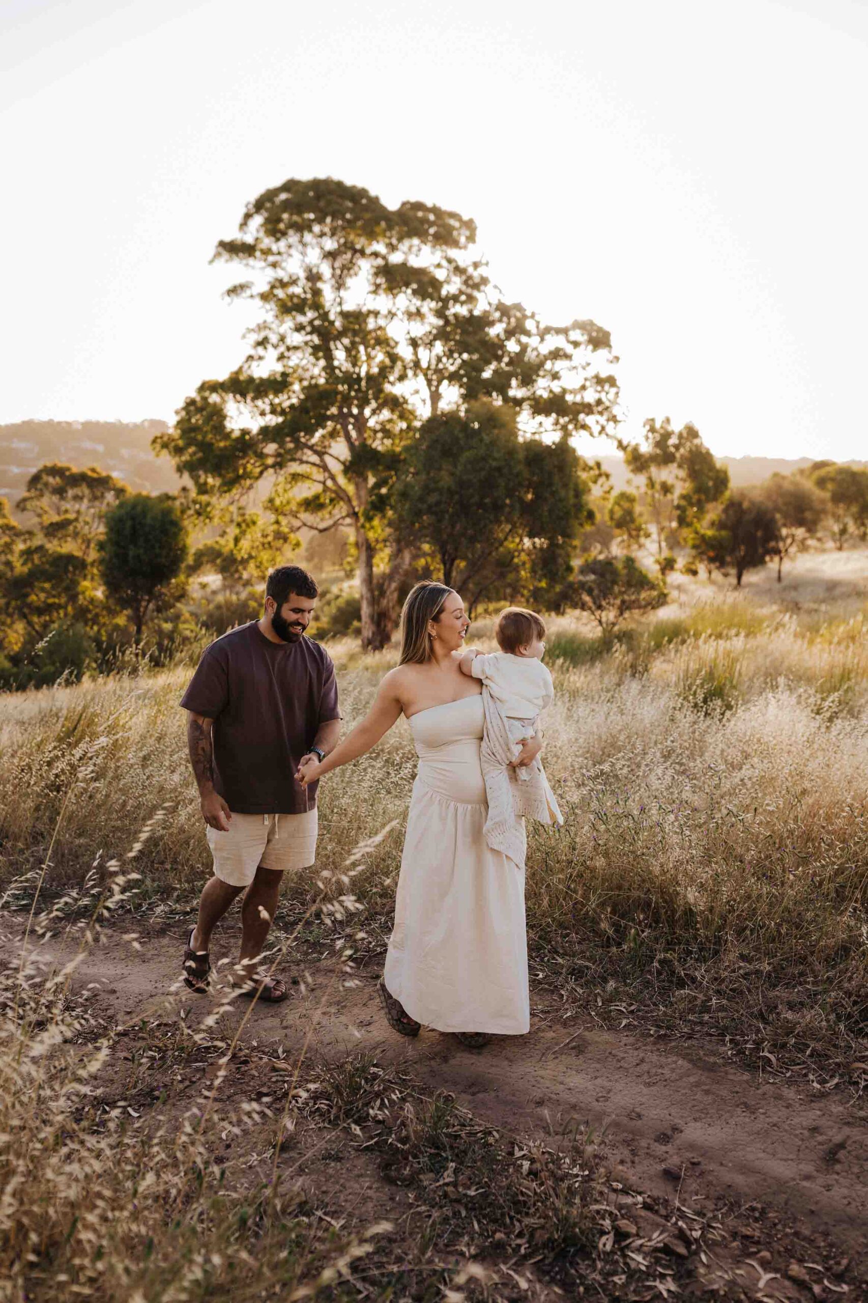 An Adelaide family of 3 walking together in a field.