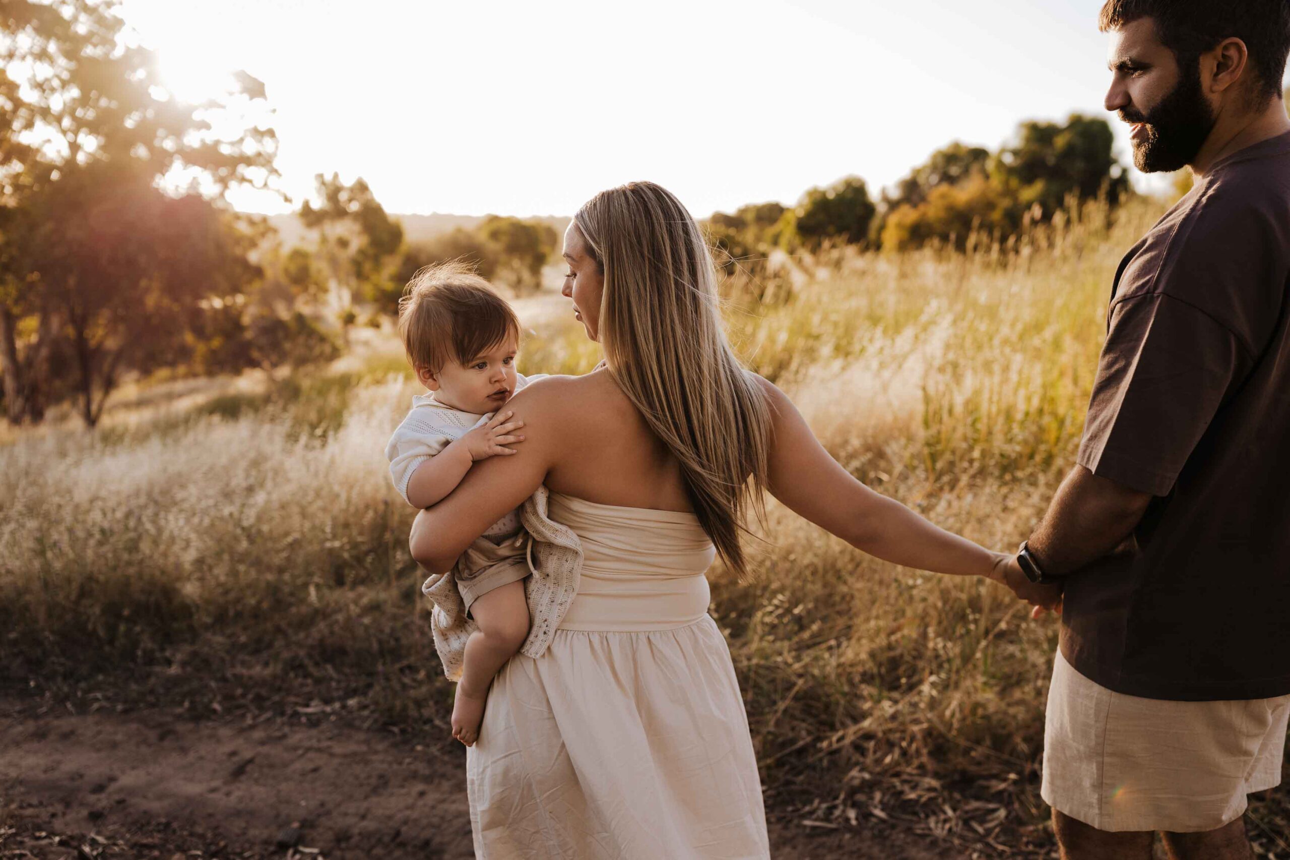 An Adelaide family of 3 walking together in a field.