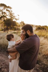An Adelaide family of 3 standing and hugging each other in a field.