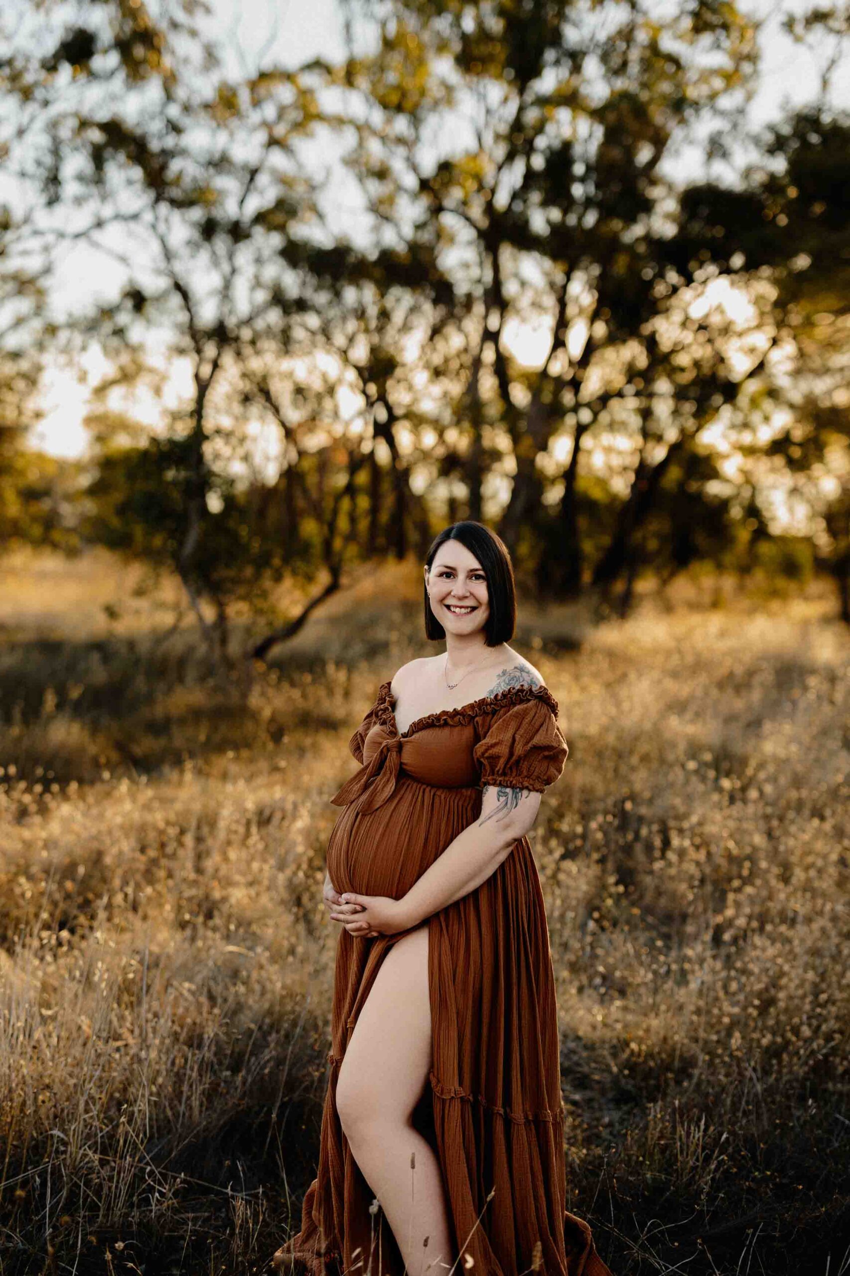 A pregnant mum from Adelaide smiling while wearing a rust dress at sunset.