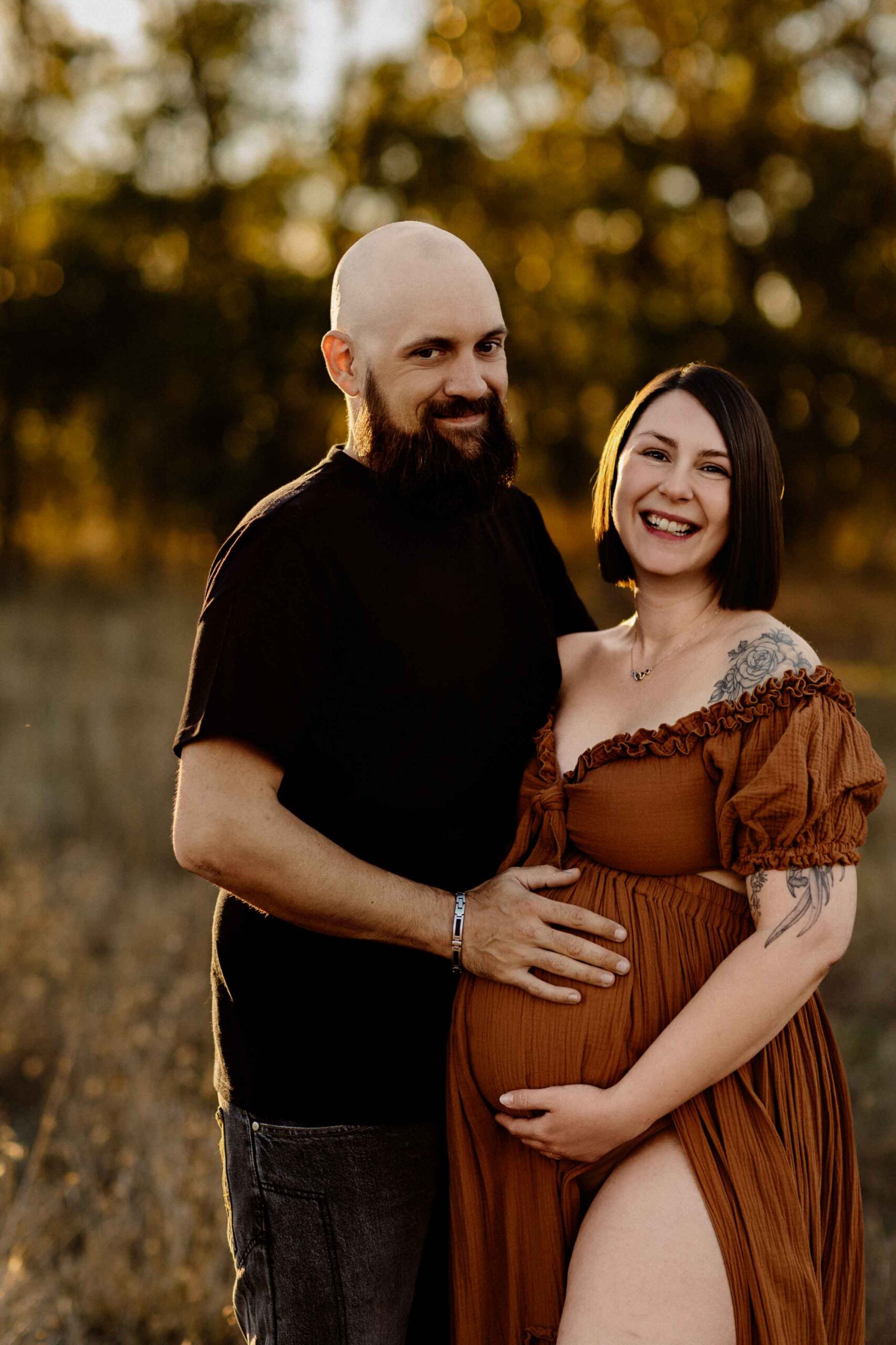 A couple from Adelaide cuddling with their hands on the woman's pregnant belly at sunset.