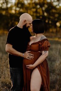 A couple from Adelaide facing each other with their hands on the woman's pregnant belly.