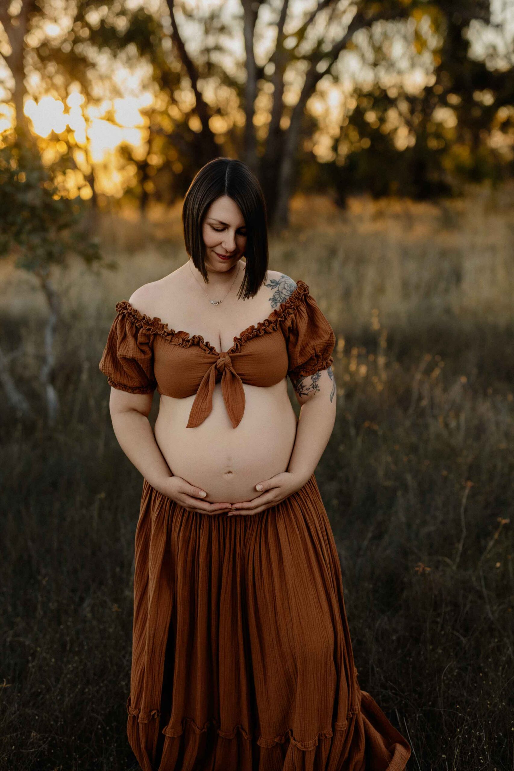 A mum from Adelaide looking at her pregnant belly at sunset.