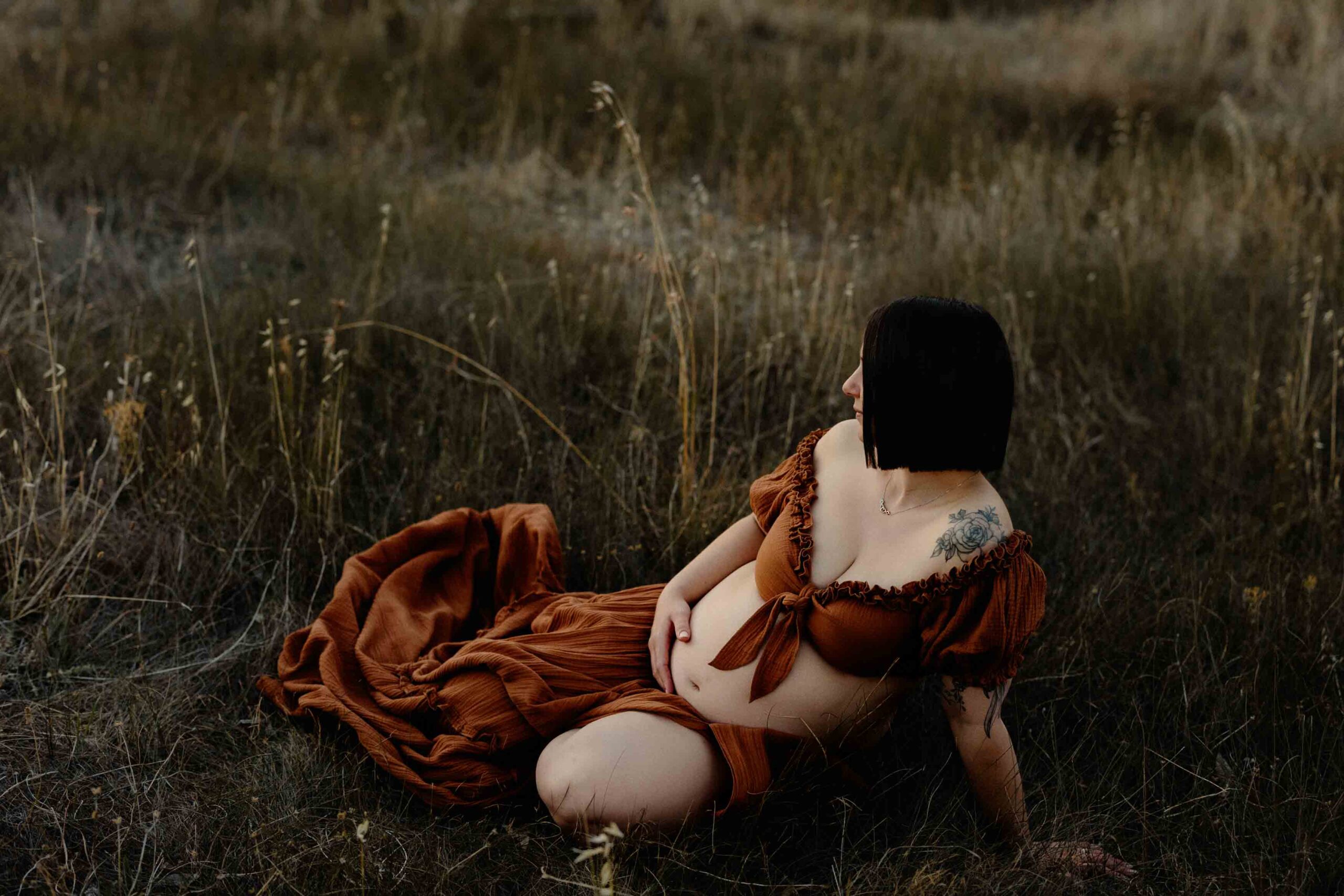 A pregnant mum from Adelaide sitting in grass wearing a rust dress during a maternity session.