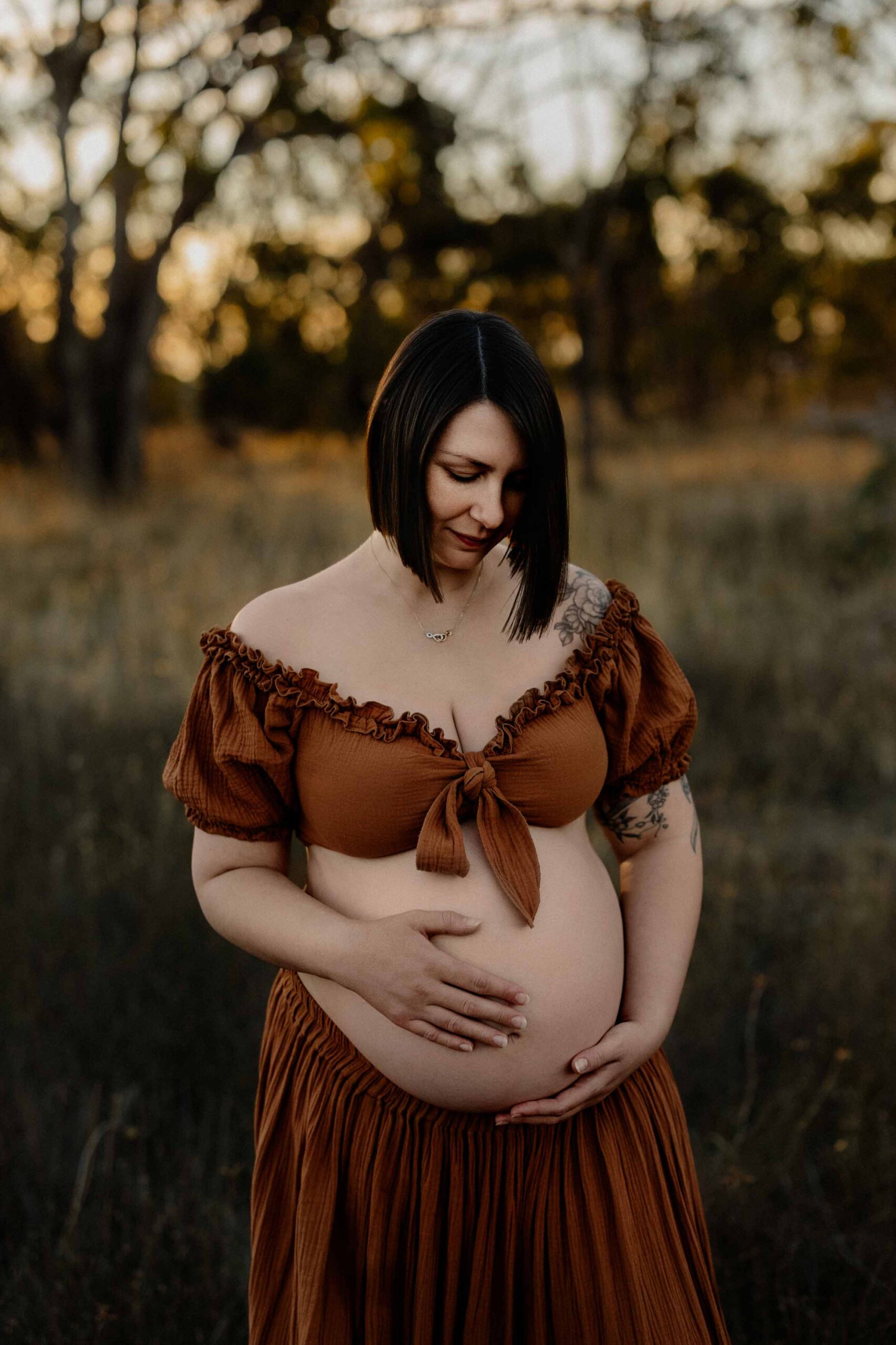 A mum from Adelaide looking at her pregnant belly wearing a 2 piece rust outfit.