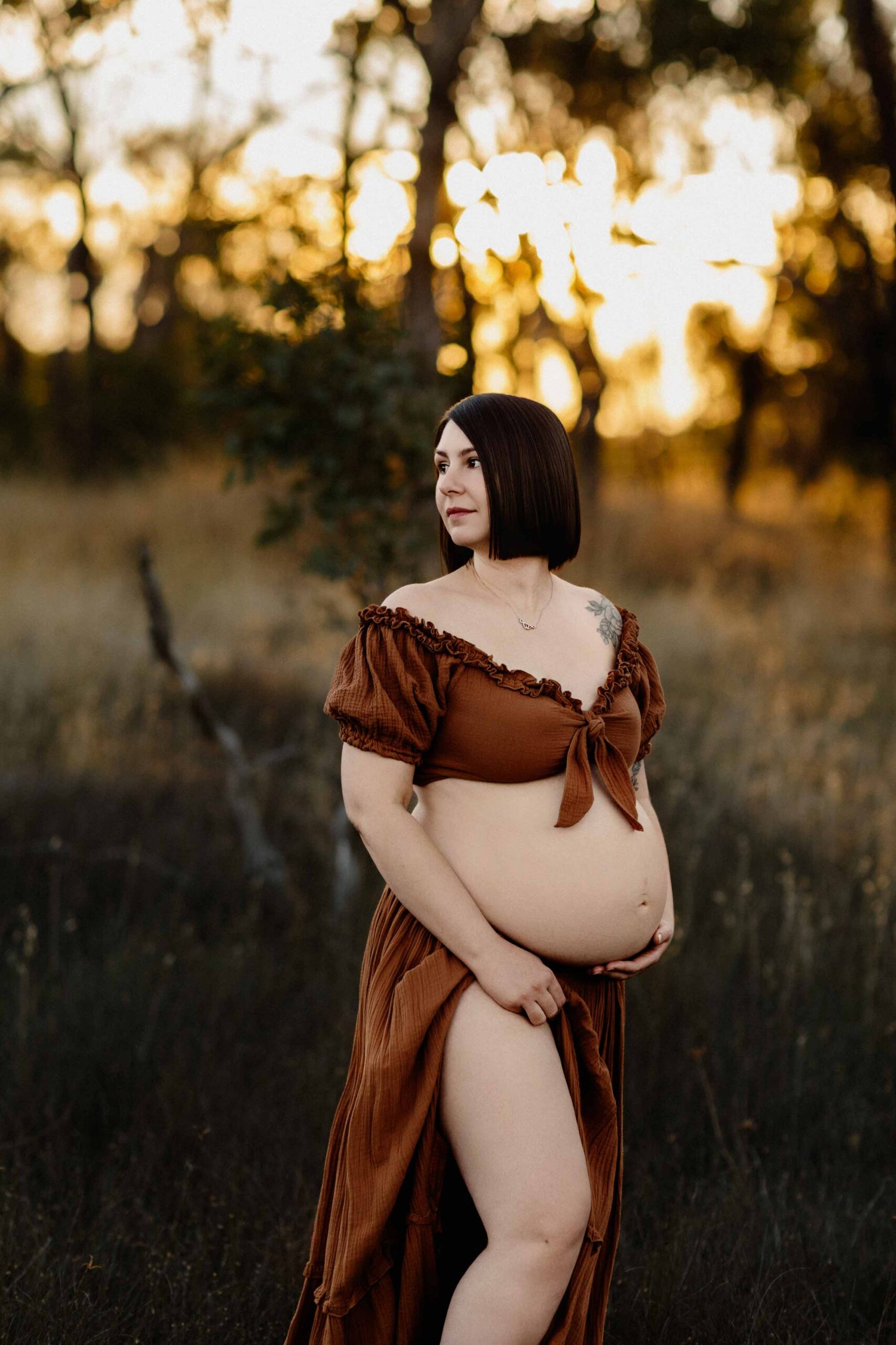 A mum from Adelaide looking to the side wearing a rust dress at sunset.
