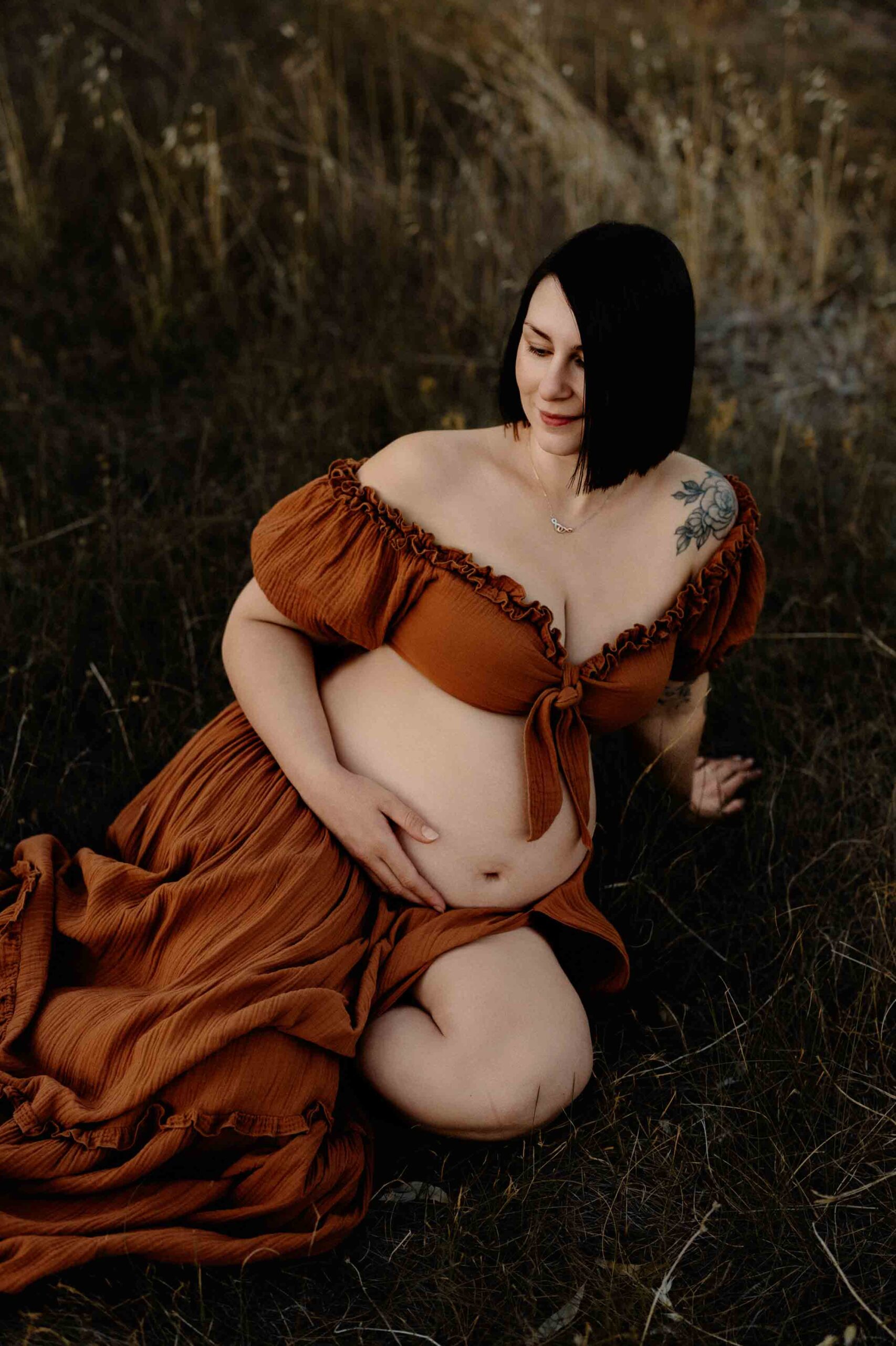 A pregnant mum from Adelaide sitting in grass wearing a rust dress.