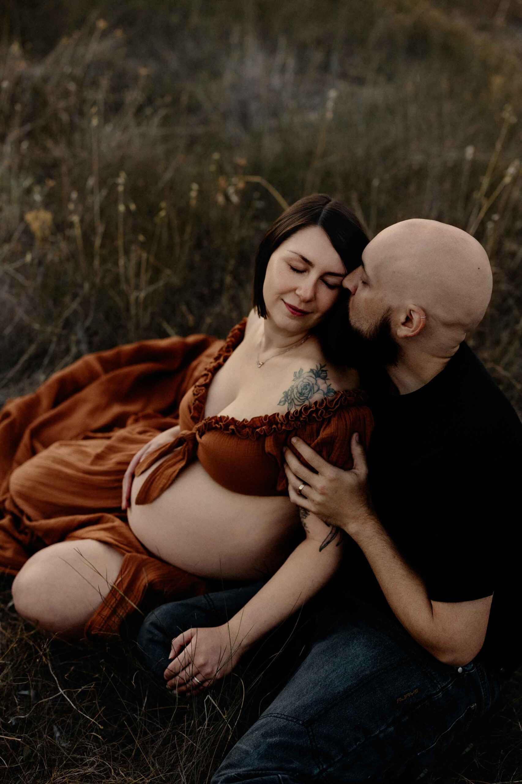A pregnant mother and her partner sitting in grass.