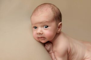 An awake Adelaide baby laying on a beige background is looking at the camera
