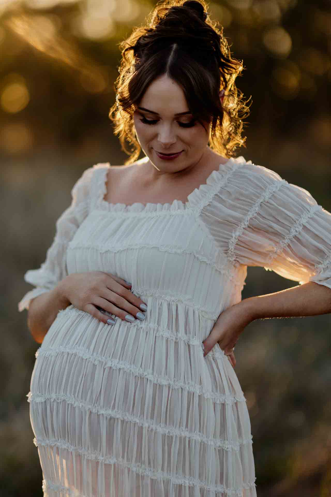 A pregnant mother in a white dress looking down  at a maternity session in Adelaide.