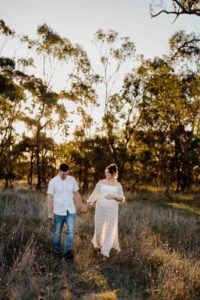 A pregnant mother and her partner walking in a field at a maternity session in Adelaide.
