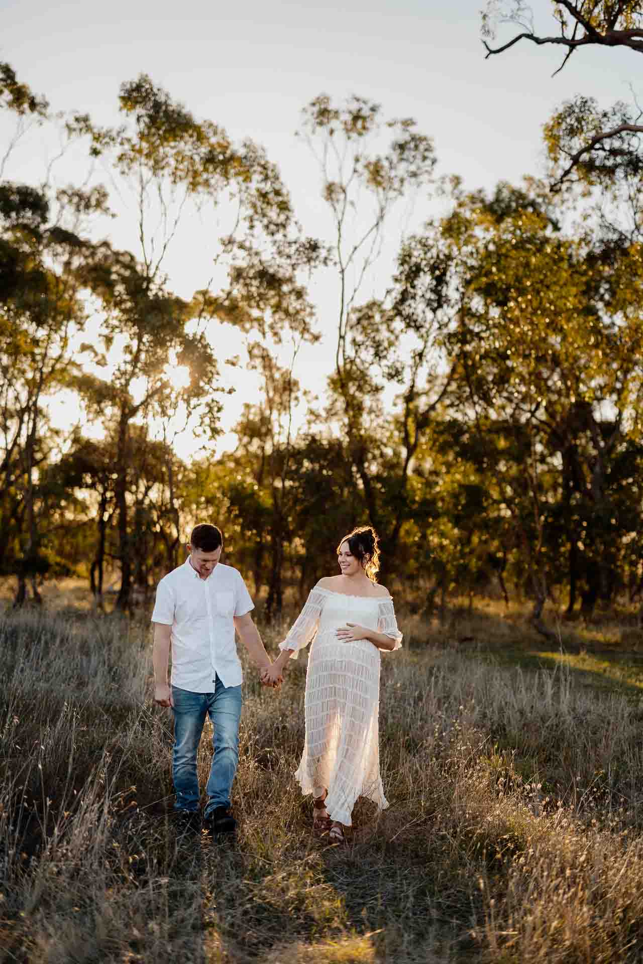 A pregnant mother and her partner walking in a field at a maternity session in Adelaide.