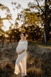 A pregnant mother in a white dress standing in the sun at a maternity session in Adelaide.