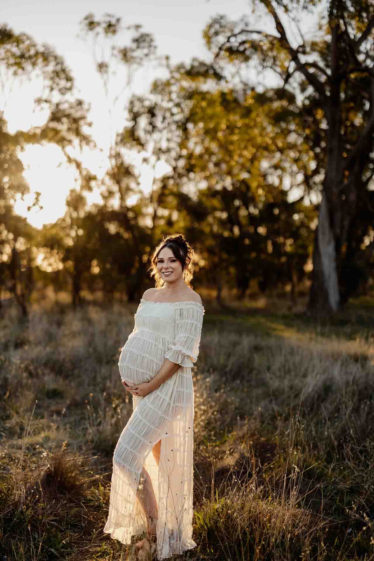 A pregnant mother in a white dress standing in the sun at a maternity session in Adelaide.