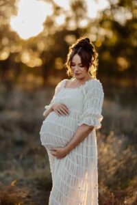 A pregnant mother in a white dress looking at her tummy at a maternity session in Adelaide.