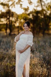 A pregnant mother in a white dress smiling at a maternity session in Adelaide.