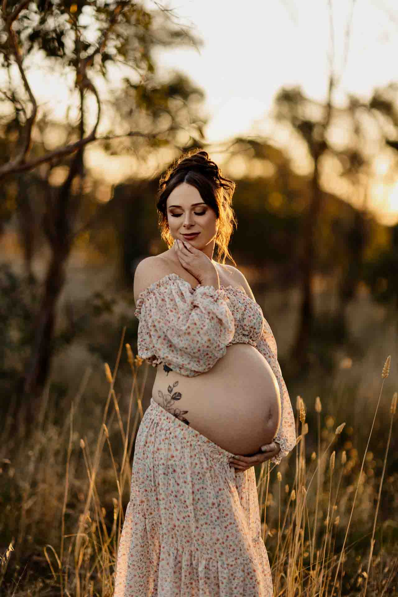 A pregnant mother wearing a 2 piece floral set back lit by the sun at a maternity session in Adelaide.