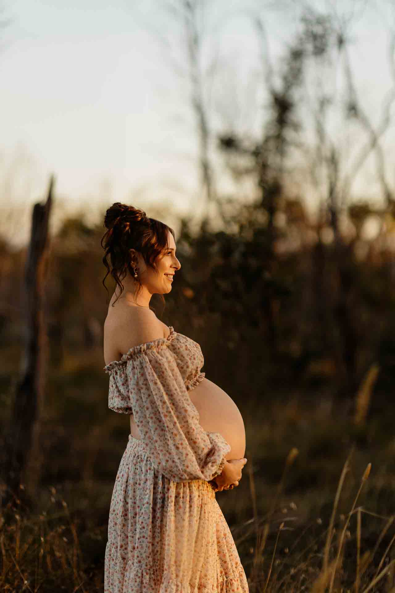 A pregnant mother wearing a 2 piece floral set smiling in the sun at a maternity session in Adelaide.